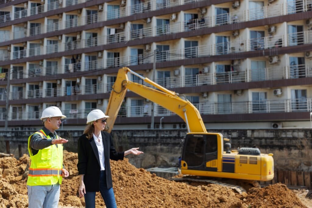 Two construction professionals discuss and point toward excavation activity with a large dirt pile
